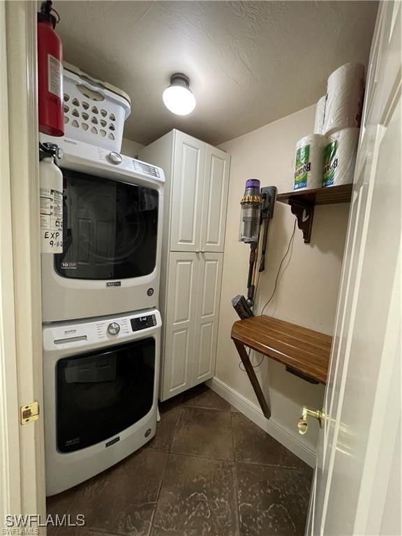 laundry room with cabinets, stacked washer / dryer, and dark tile patterned flooring