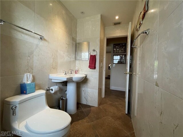 bathroom with tile patterned floors, toilet, and tile walls