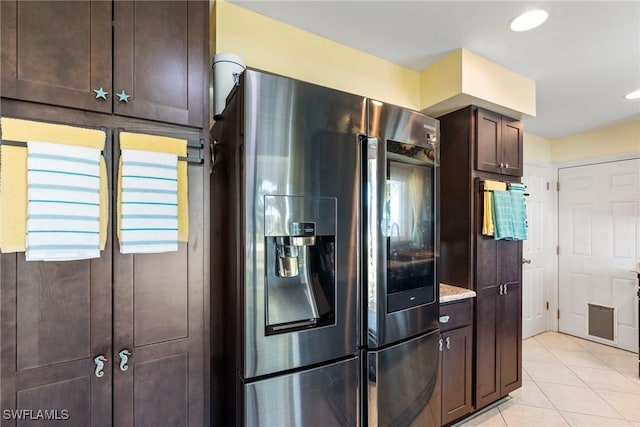 kitchen with dark brown cabinetry, light tile patterned floors, light stone counters, and stainless steel fridge