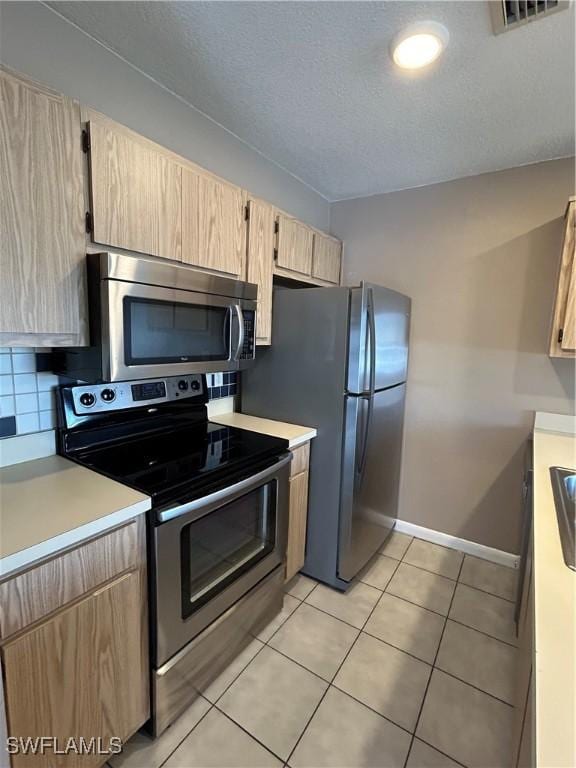 kitchen with light tile patterned floors, stainless steel appliances, tasteful backsplash, a textured ceiling, and light brown cabinetry