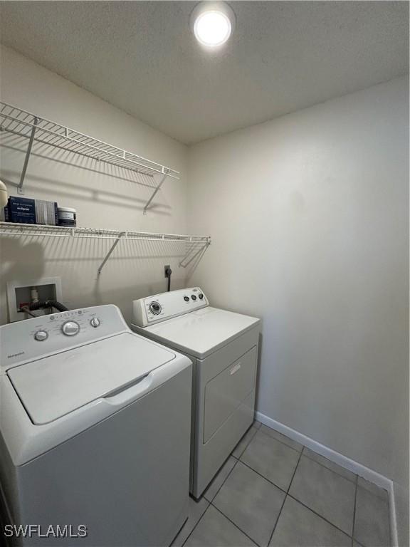 laundry area with light tile patterned floors, washer and clothes dryer, and a textured ceiling