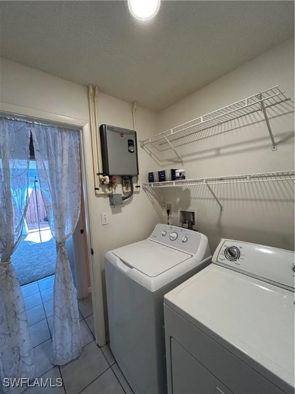 clothes washing area with water heater, a textured ceiling, washer and dryer, and light tile patterned floors