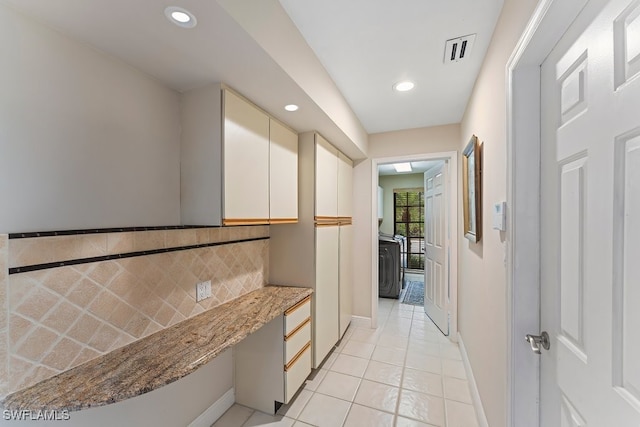 kitchen with white cabinetry, backsplash, built in desk, light stone countertops, and light tile patterned flooring