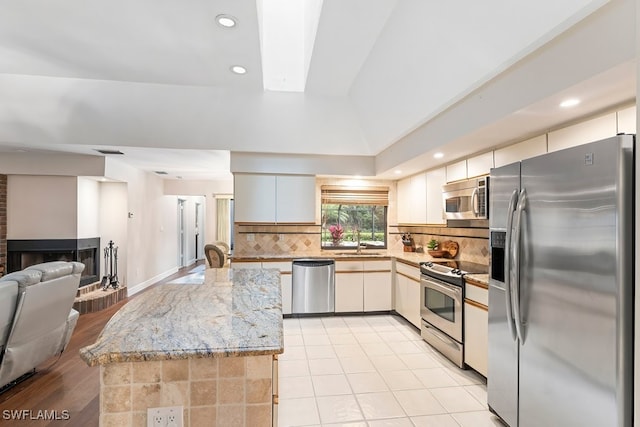 kitchen featuring sink, a brick fireplace, stainless steel appliances, light stone countertops, and decorative backsplash