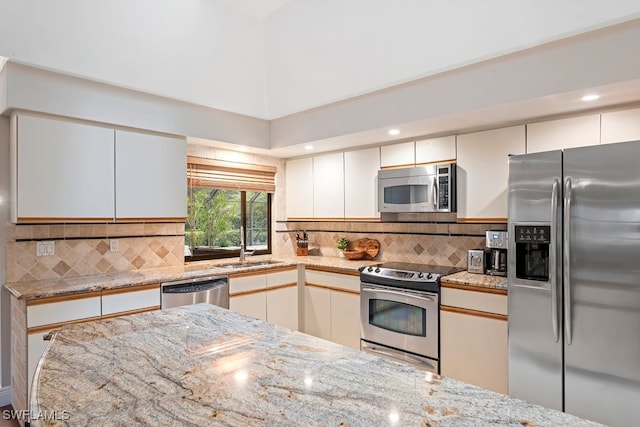 kitchen featuring light stone counters, white cabinetry, stainless steel appliances, and decorative backsplash