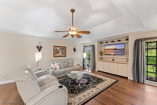 living room featuring ceiling fan, dark hardwood / wood-style flooring, and a tray ceiling