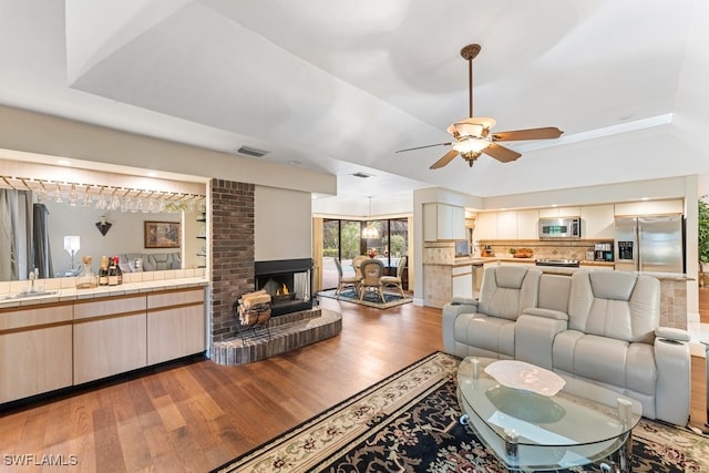 living room with sink, dark hardwood / wood-style flooring, ceiling fan, a tray ceiling, and a brick fireplace