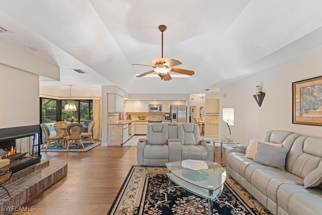 living room featuring hardwood / wood-style flooring, ceiling fan with notable chandelier, and a multi sided fireplace