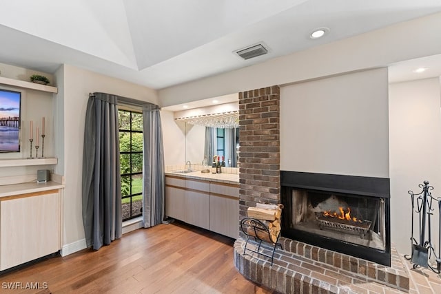 interior space with a brick fireplace, sink, and light hardwood / wood-style flooring