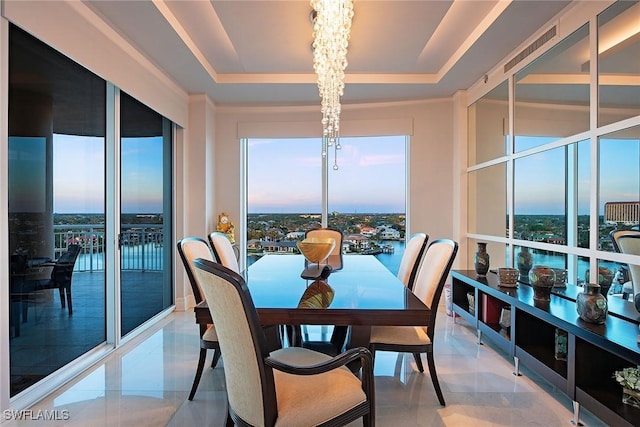 dining area with a water view, a tray ceiling, and a chandelier