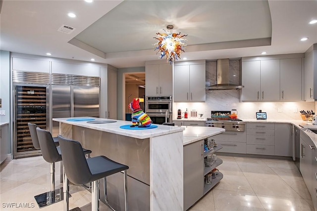 kitchen with gray cabinetry, a raised ceiling, wall chimney exhaust hood, and a kitchen island