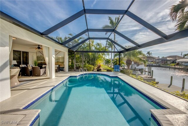 view of swimming pool with ceiling fan, a water view, glass enclosure, and a patio