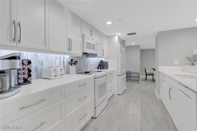 kitchen with sink, white appliances, light stone counters, white cabinets, and decorative backsplash