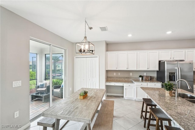 kitchen with sink, white cabinetry, light stone counters, stainless steel fridge, and pendant lighting