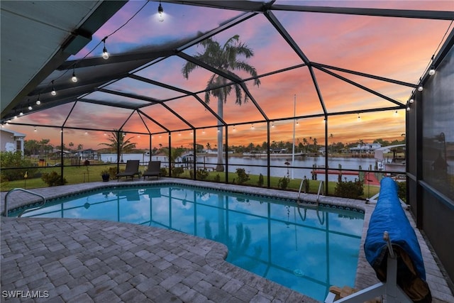 pool at dusk featuring a patio area, glass enclosure, and a water view