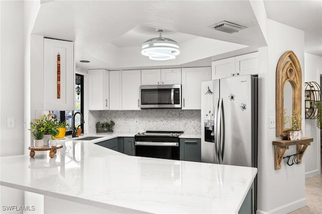 kitchen featuring sink, white cabinetry, appliances with stainless steel finishes, a tray ceiling, and kitchen peninsula