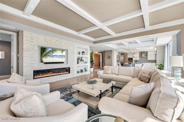 living room featuring beamed ceiling, a notable chandelier, coffered ceiling, wood finished floors, and a stone fireplace