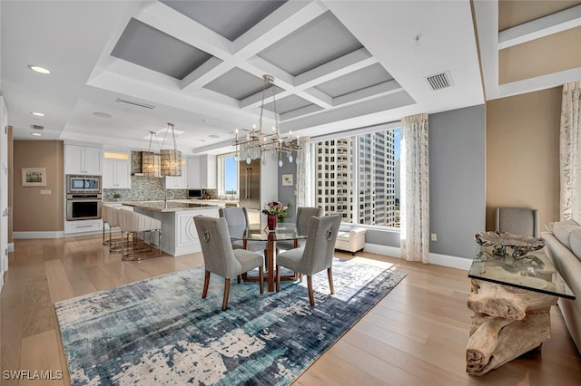 dining space featuring an inviting chandelier, coffered ceiling, sink, and light wood-type flooring