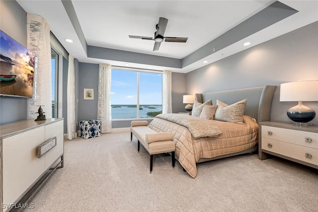 carpeted bedroom with a water view, ceiling fan, and a tray ceiling