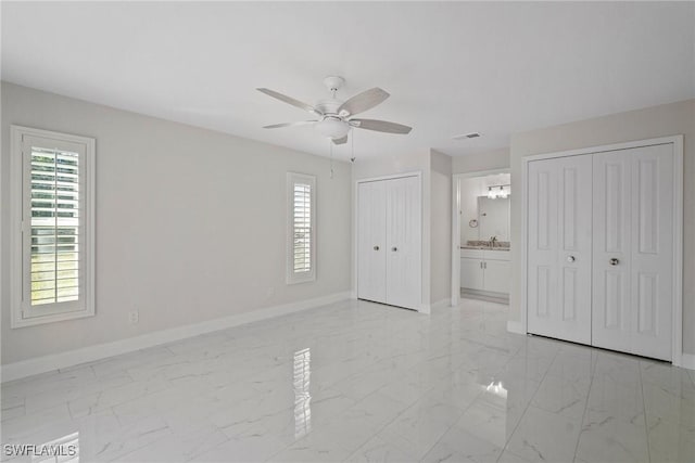 unfurnished bedroom with ceiling fan, ensuite bath, and multiple closets