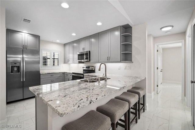 kitchen featuring a kitchen bar, sink, gray cabinetry, appliances with stainless steel finishes, and kitchen peninsula