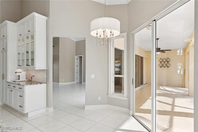 interior space featuring ceiling fan with notable chandelier, light tile patterned floors, a towering ceiling, and baseboards