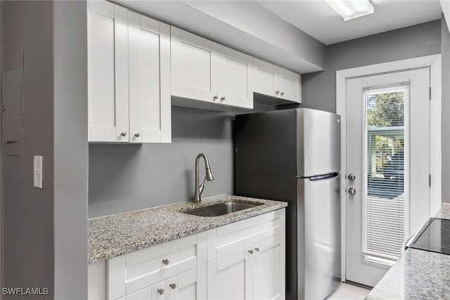 kitchen featuring stainless steel fridge, light stone countertops, sink, and white cabinets