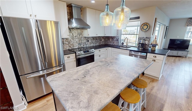 kitchen featuring sink, appliances with stainless steel finishes, white cabinets, decorative light fixtures, and wall chimney exhaust hood