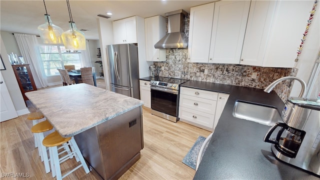 kitchen featuring white cabinetry, wall chimney range hood, pendant lighting, and appliances with stainless steel finishes