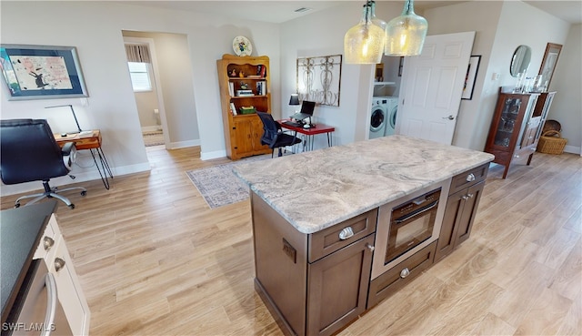 kitchen with decorative light fixtures, a center island, light hardwood / wood-style floors, light stone countertops, and washer and clothes dryer