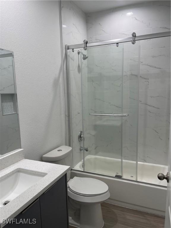 full bathroom featuring bath / shower combo with glass door, hardwood / wood-style floors, vanity, and toilet