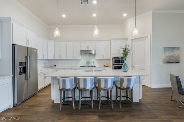 kitchen featuring pendant lighting, stainless steel appliances, an island with sink, and white cabinets