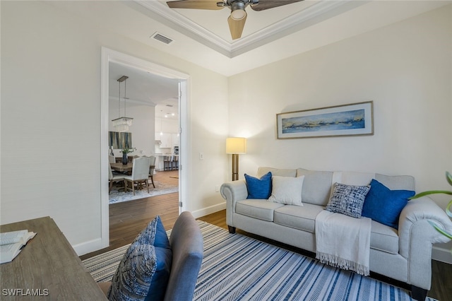 living room with a tray ceiling, ornamental molding, hardwood / wood-style floors, and ceiling fan