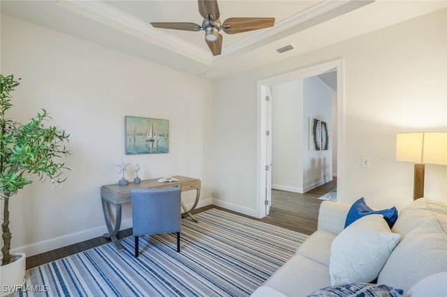 office space featuring a tray ceiling, ornamental molding, ceiling fan, and dark hardwood / wood-style flooring