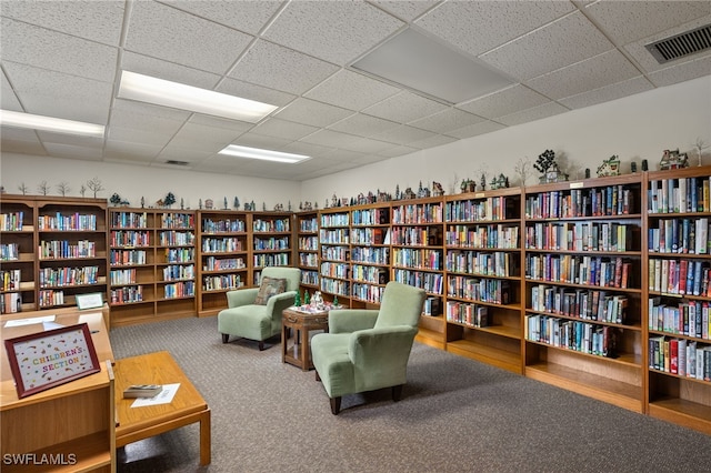 living area featuring a drop ceiling and carpet flooring