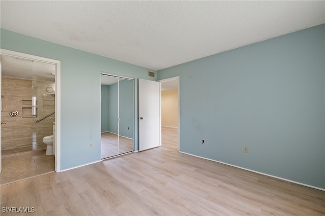 unfurnished bedroom featuring ensuite bathroom, a closet, a textured ceiling, and light wood-type flooring