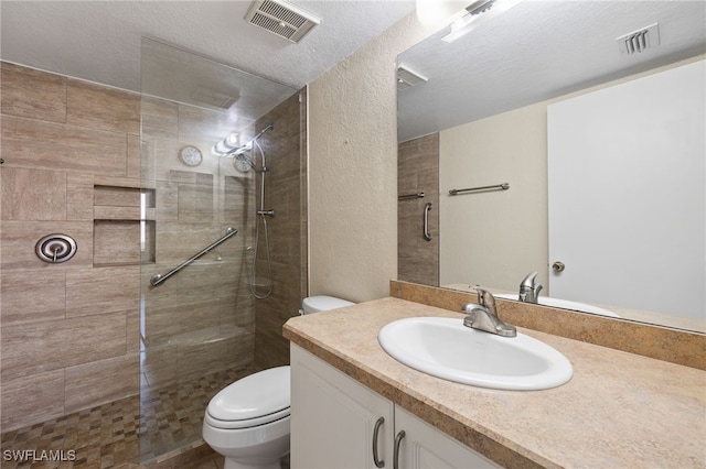 bathroom with vanity, a tile shower, a textured ceiling, and toilet