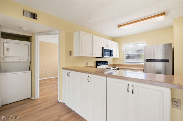 kitchen with stainless steel refrigerator, stacked washing maching and dryer, range with electric cooktop, a textured ceiling, and white cabinets