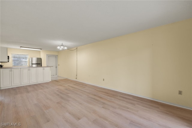 unfurnished living room featuring an inviting chandelier and light wood-type flooring