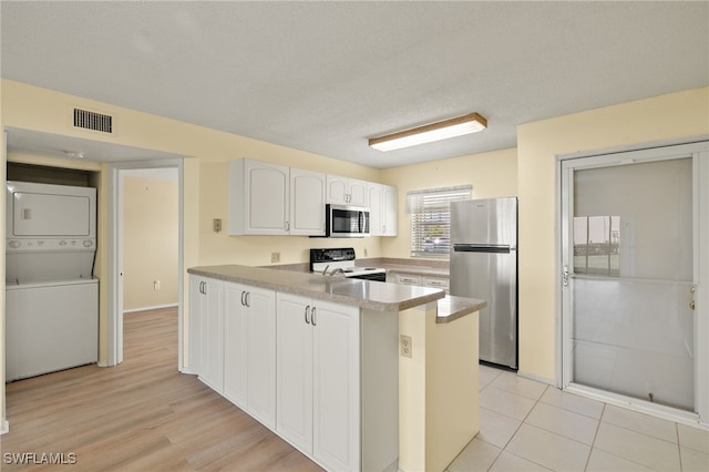 kitchen with appliances with stainless steel finishes, white cabinetry, stacked washer and dryer, kitchen peninsula, and a textured ceiling