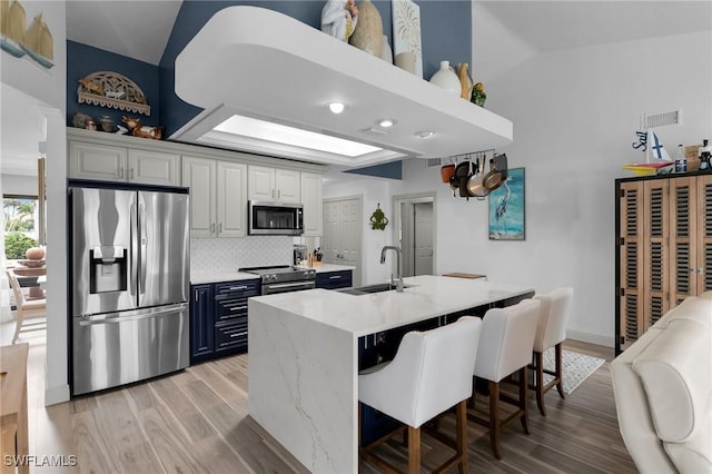 kitchen featuring sink, a breakfast bar area, white cabinetry, light stone counters, and appliances with stainless steel finishes