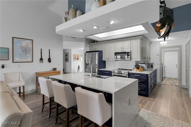 kitchen featuring sink, appliances with stainless steel finishes, gray cabinetry, backsplash, and a kitchen bar