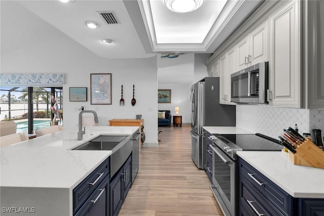 kitchen with appliances with stainless steel finishes, white cabinetry, an island with sink, sink, and light wood-type flooring