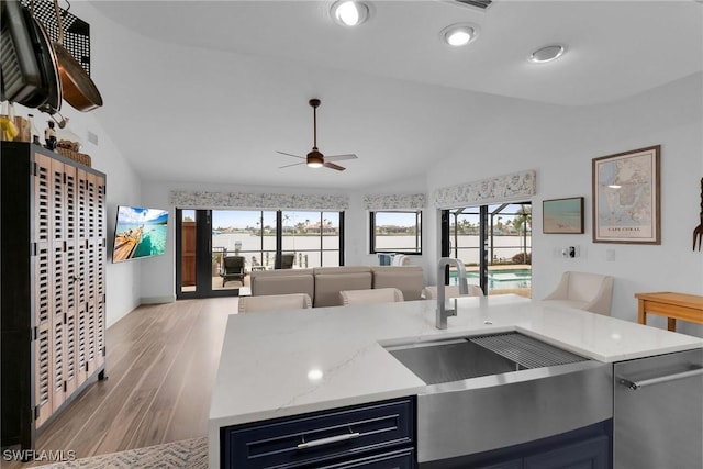 kitchen featuring blue cabinetry, sink, light stone counters, vaulted ceiling, and light hardwood / wood-style floors