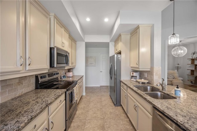 kitchen with pendant lighting, sink, appliances with stainless steel finishes, light stone counters, and cream cabinetry