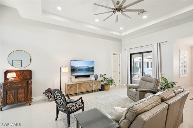 living room featuring a raised ceiling, a high ceiling, and ceiling fan