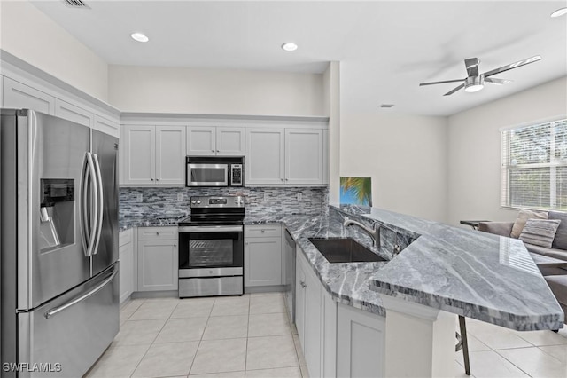 kitchen featuring light stone counters, stainless steel appliances, a kitchen breakfast bar, and kitchen peninsula