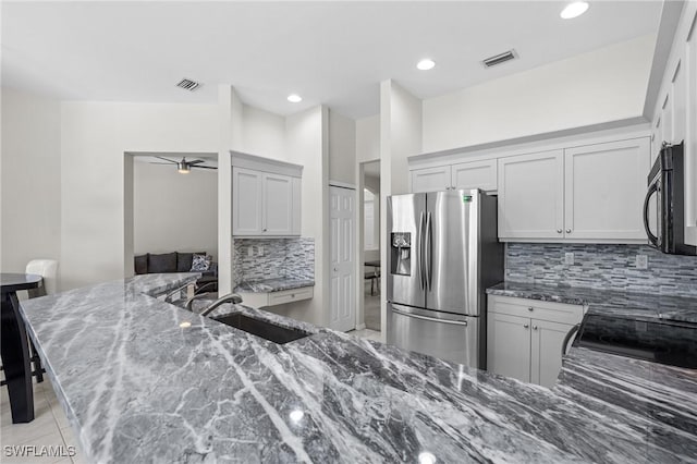 kitchen with sink, stainless steel fridge, stone counters, ceiling fan, and decorative backsplash