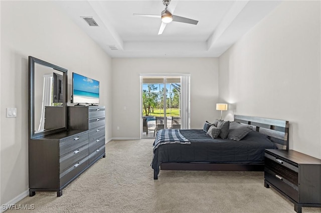 carpeted bedroom featuring access to exterior, a tray ceiling, and ceiling fan