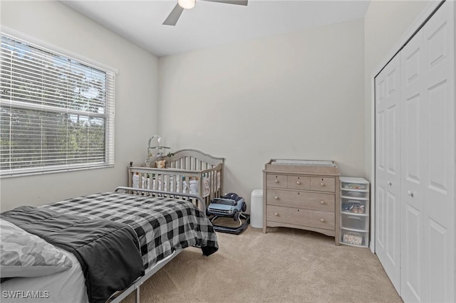 bedroom featuring light colored carpet, ceiling fan, and a closet